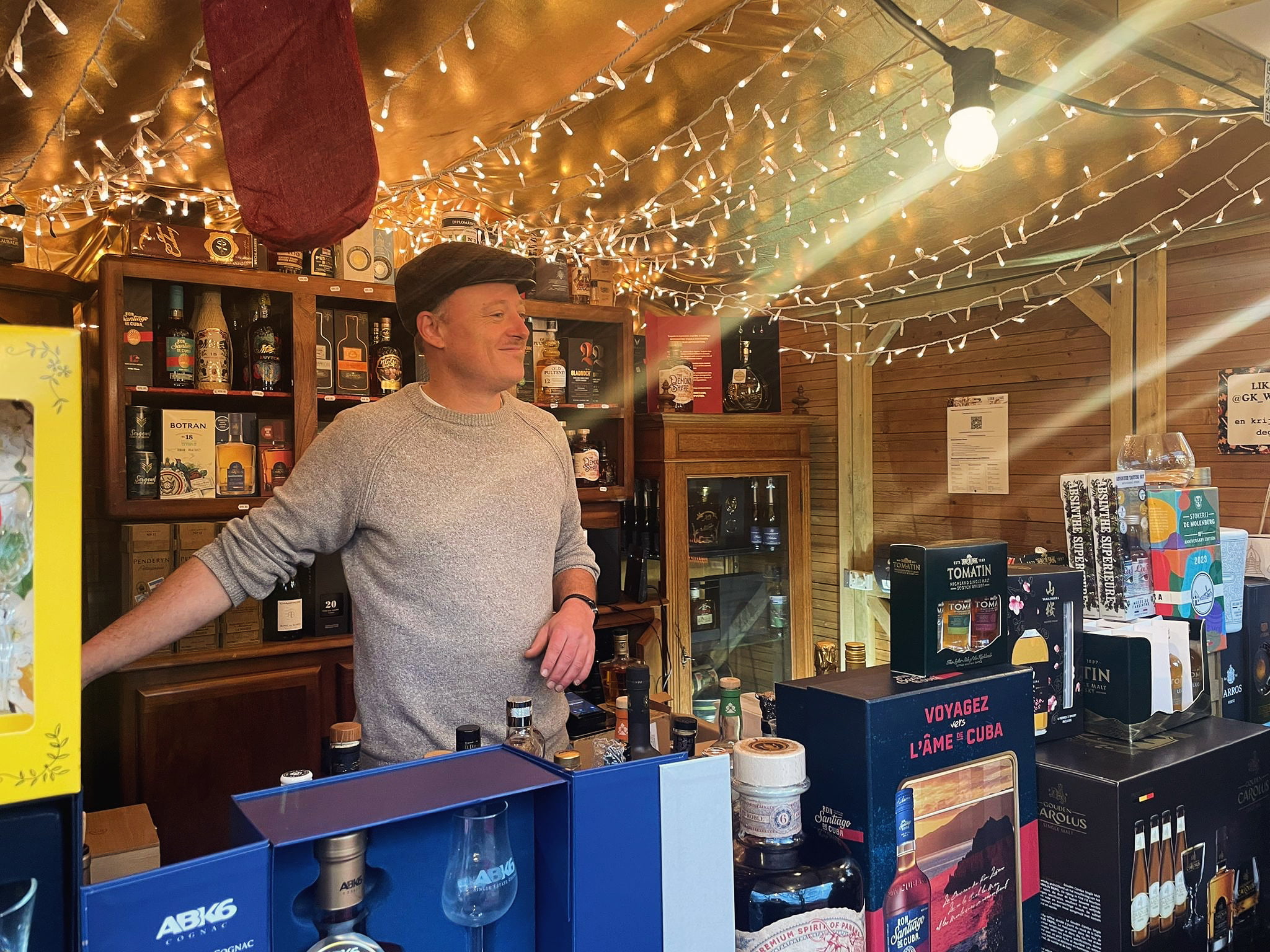 Korneel achter de toonbank van zijn drankenkraam, omringd door rum, whisky en cognac