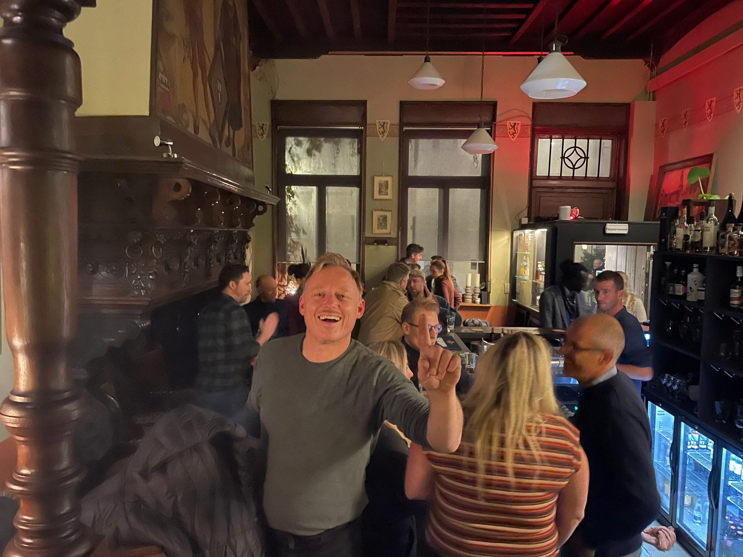 Korneel lachend in een drukke horecazaak, tussen de gasten en de flessen achter de bar